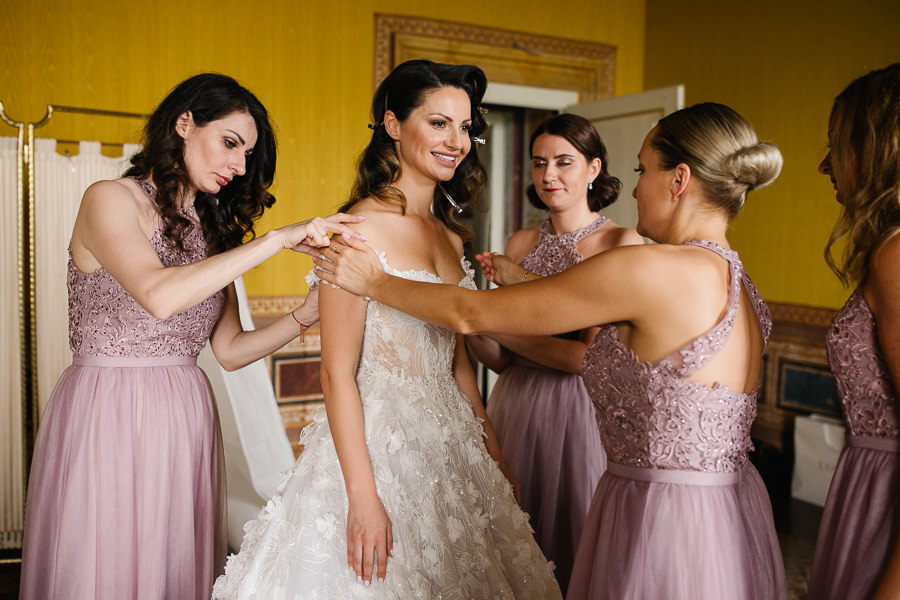 Bridesmaids helping the bride to put her dress on